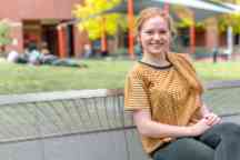 Young woman sits on bench smiling at camera