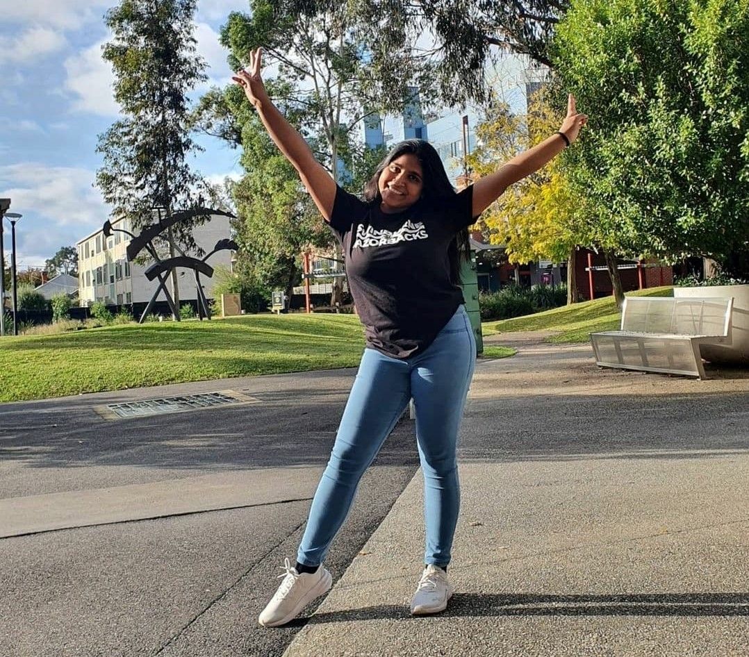 Sohani stands in a happy 'Y' pose on the green grounds of Swinburne's Hawthorn campus. 