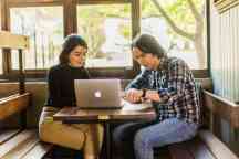 Students in a cafe discussing an assignment on a laptop