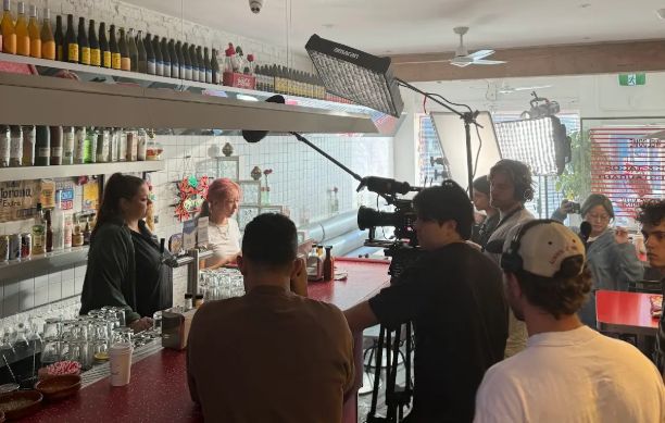 Swinburne alumni on the set of the ‘Even Better’ music video shoot, surrounded by camera crew