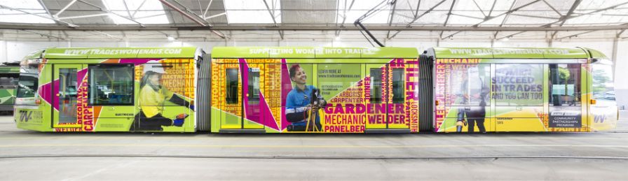 The full tram design, with real tradeswomen in the foreground against a bright, geometric background of green, pink and yellow. 