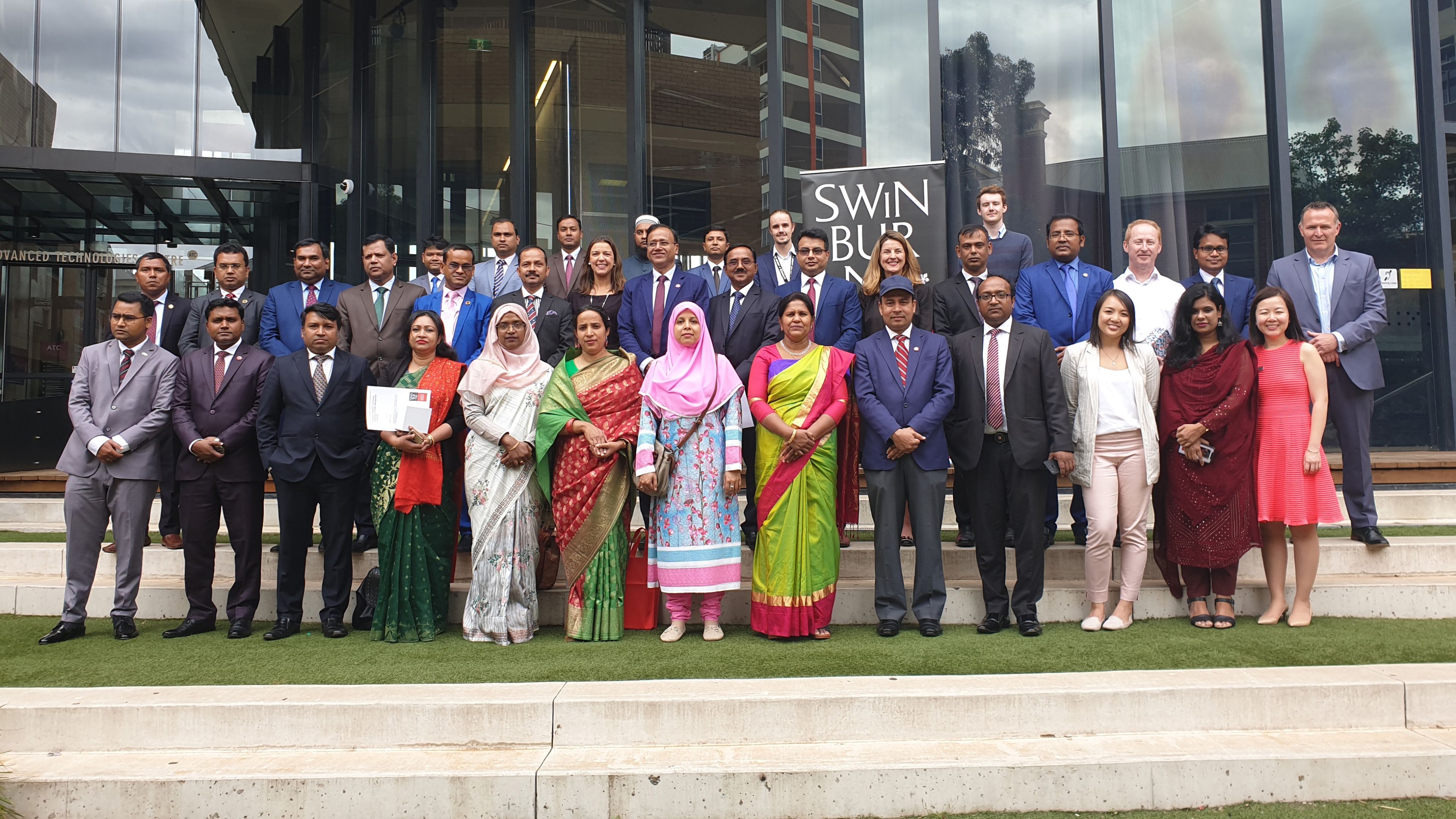 A large group of people standing outside a university building in front of the Swinburne logo.