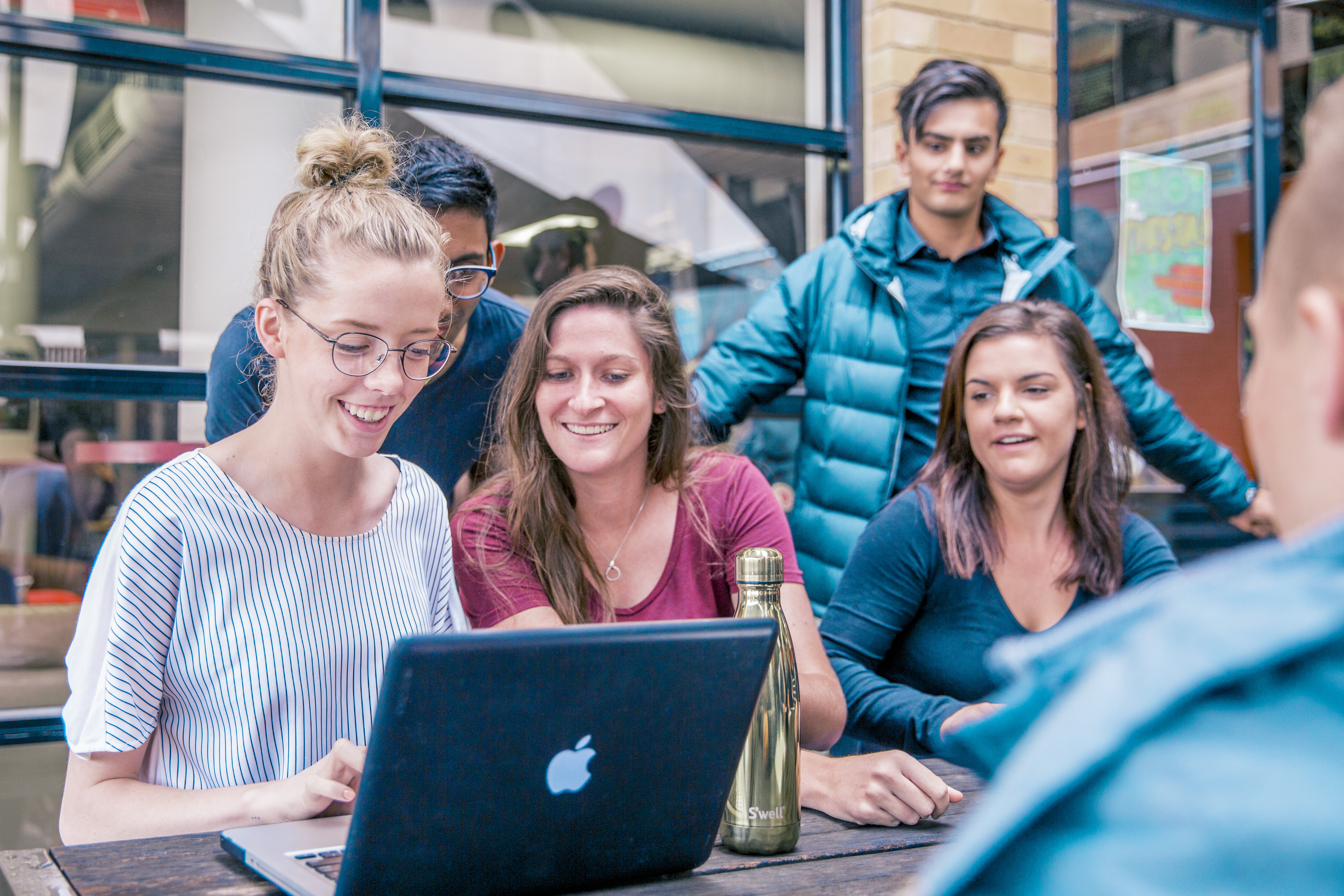 A group of students smiling and looking at a laptop together.
