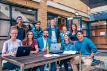Student ambassadors sit at a table and smile to camera sitting on a bench