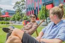 Male and female students sit on deck chairs in the garden in the sun