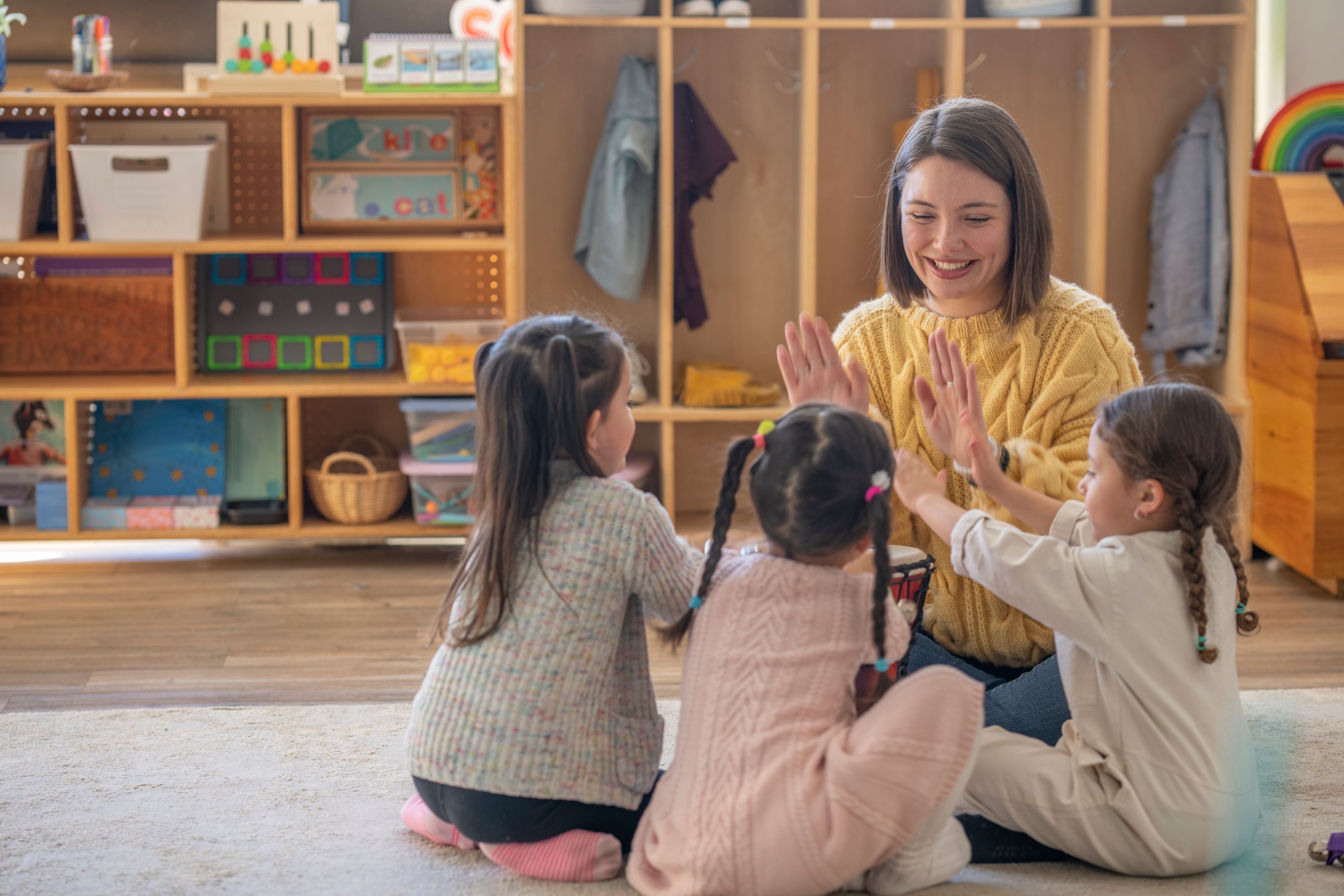 Kindergarten students with their early childhood teacher sitting on the ground playing.