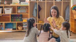 Kindergarten kids with their early childhood teacher sitting on the ground playing - STOCK - V2