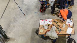 Plumbing apprentices using tools at a workshop table.