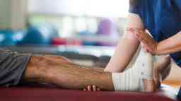 A female occupational therapist holding leg and foot of a male patient with a bandage in his ankle.