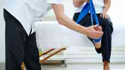 Female patient doing some special leg stretching exercises with under supervision in a medical room.