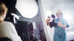 A young woman wearing a beanie films with a smartphone rig in a studio with professional lighting.