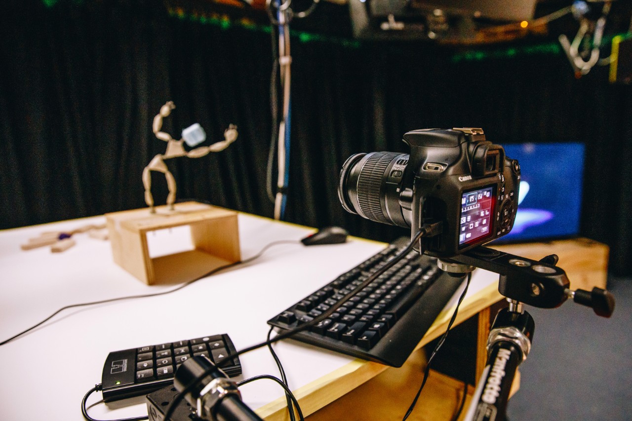 Digital camera setup upon stand ready to capture wooden figurine in blurred background