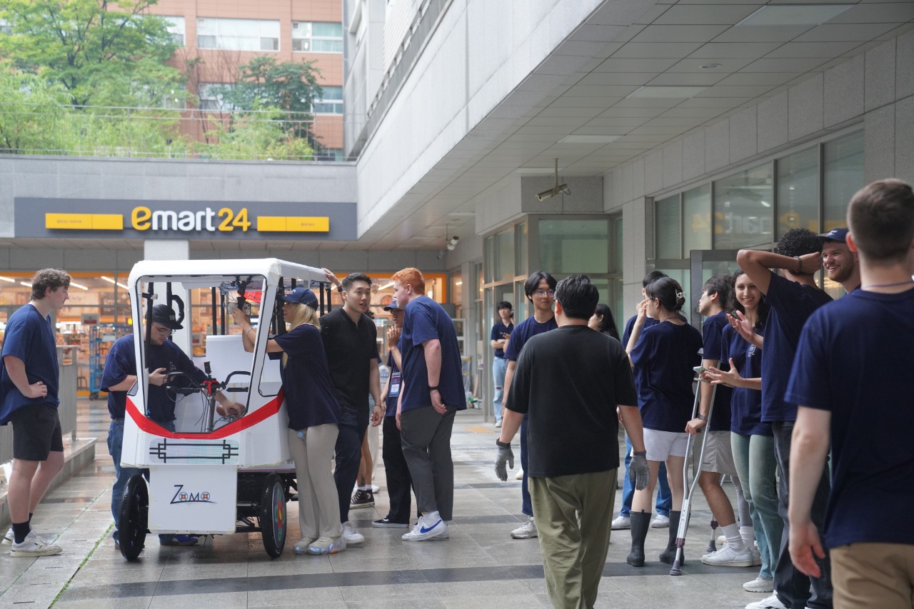 A large group of students congregating outside around a prototype four-wheeled mobility device