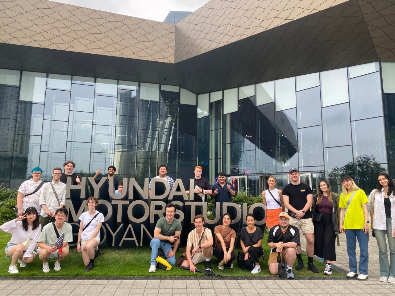 A group of students and a lecturer stand around the large 3D Hyundai Motor studio sign