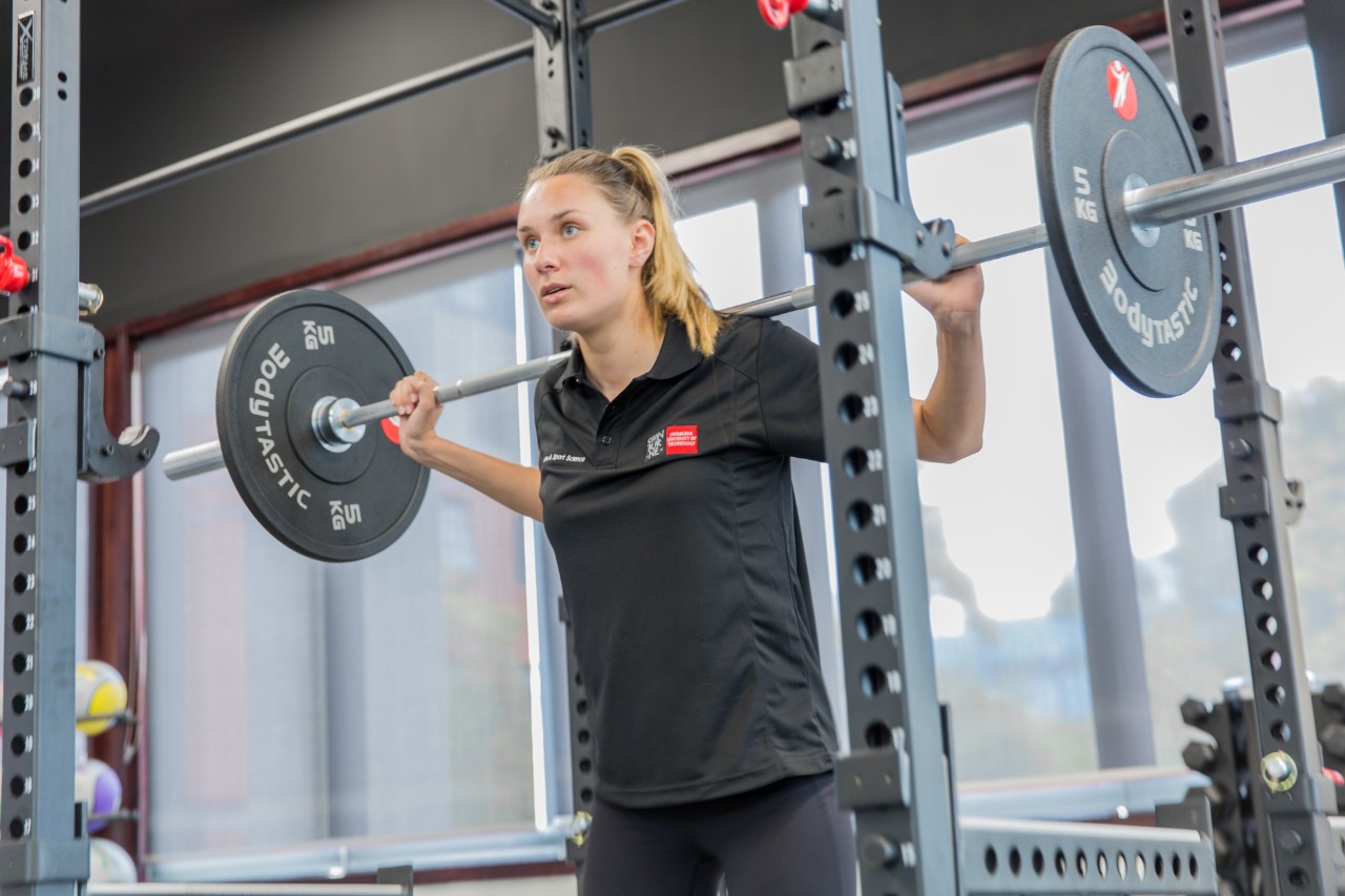 Mid shot of female student in Swinburne apparel doing 10kg squats